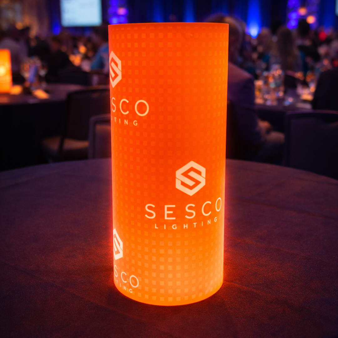 Orange cylindrical light with 'Sesco Lighting' branding on a table in a dimly lit room.